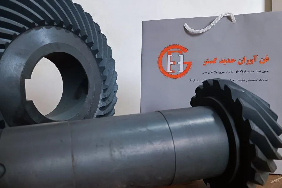چرخدنده مخروطی مارپیچ و شفت پینیون، کنار کیسهای با لوگو و نام فنآوران حدید گستر